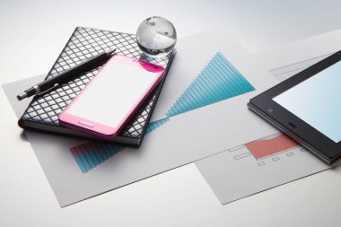 Beyaz arkaplanda akıllı telefon, dijital tablet, not defteri, kalem, cam küre ve iş haritalarının yakın plan görüntüsü     