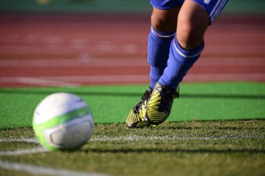 Bir futbolcu sahada futbol topunu tekmeliyor.