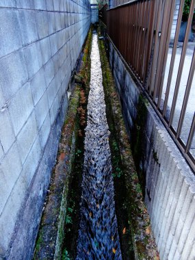 Kentsel duvarlar arasında akan beton drenaj kanalını daralt