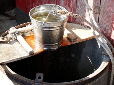 Eski kuyunun üzerinde suyla dolu metal bir kova.