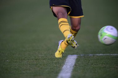 Bir futbolcu sahada futbol topunu tekmeliyor.