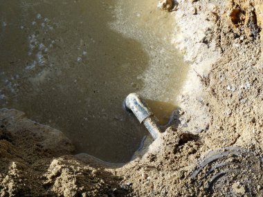 Dışarıdaki çamurlu su birikintisinden açığa çıkan metal boru.