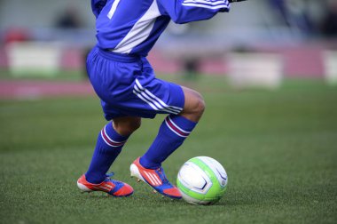 Bir futbolcu sahada futbol topunu tekmeliyor.