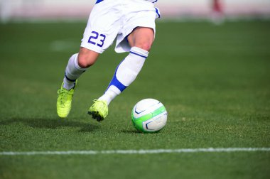 Bir futbolcu sahada futbol topunu tekmeliyor.