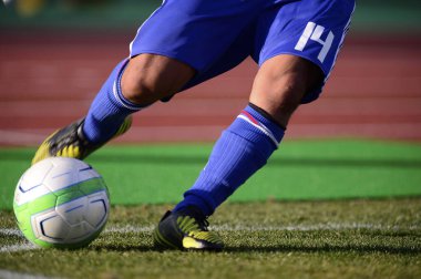 Bir futbolcu sahada futbol topunu tekmeliyor.