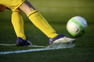 Bir futbolcu sahada futbol topunu tekmeliyor.