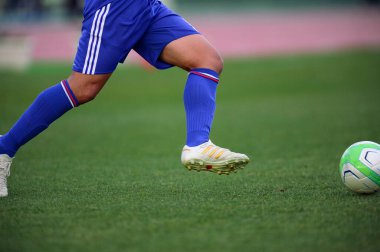 Bir futbolcu sahada futbol topunu tekmeliyor.