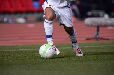 Bir futbolcu sahada futbol topunu tekmeliyor.