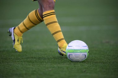 Bir futbolcu sahada futbol topunu tekmeliyor.