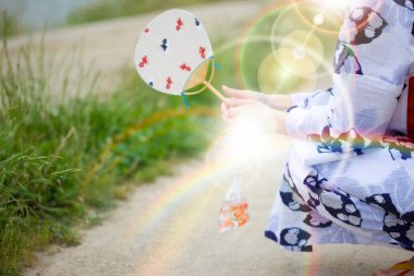 Geleneksel Japon tarzı kimono giyen ve elinde yelpaze tutan bir kadının orta kesimi.