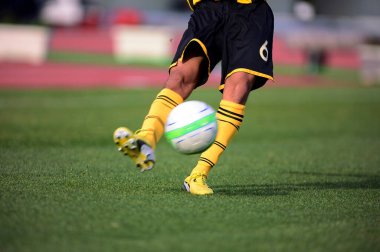 Bir futbolcu sahada futbol topunu tekmeliyor.