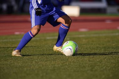 Bir futbolcu sahada futbol topunu tekmeliyor.