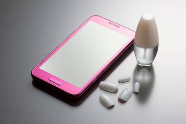 Cep telefonu ve kozmetik ürünlerinin yakın plan görüntüsü, gri arka planda tırnak cilası.          