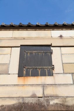 Eski taş bina duvarındaki yıpranmış siyah metal pencere panjuru.