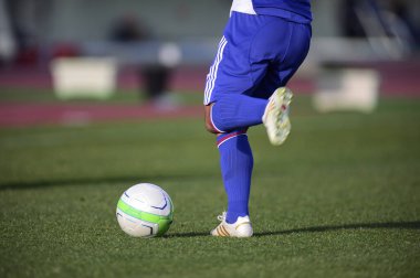 Bir futbolcu sahada futbol topunu tekmeliyor.