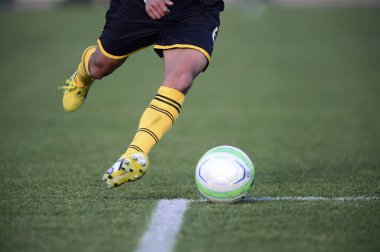 Bir futbolcu sahada futbol topunu tekmeliyor.