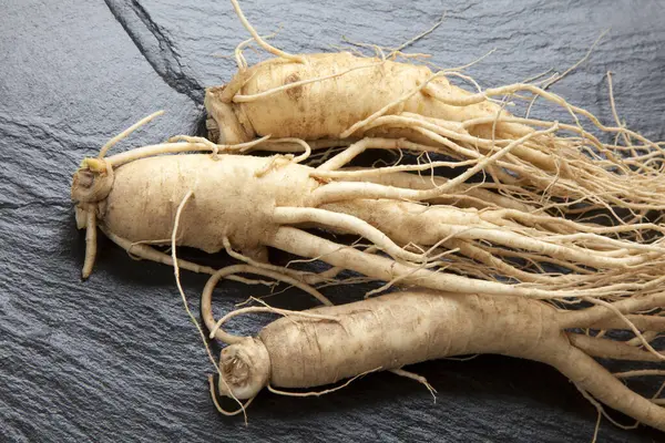 Siyah taş zemin üzerinde izole edilmiş üç ginseng kökü