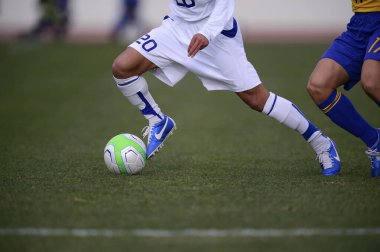 Bir futbolcu sahada futbol topunu tekmeliyor.
