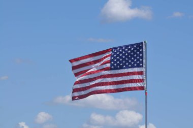 Açık mavi gökyüzünde dalgalanan Amerikan bayrağı pofuduk beyaz bulutlara karşı