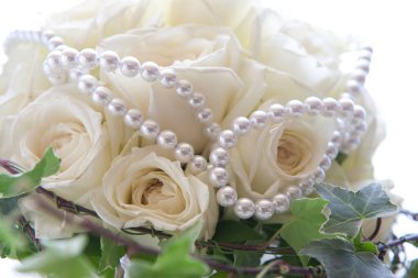 Beyaz güller, yeşil yapraklar ve incilerden oluşan güzel bir düğün buketi.    