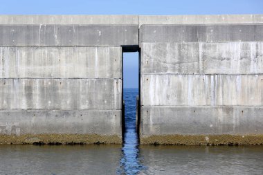 Denizde iki dalgalı su bulunan beton bir su duvarı, Hollanda 'da büyük bir endüstriyel bina.