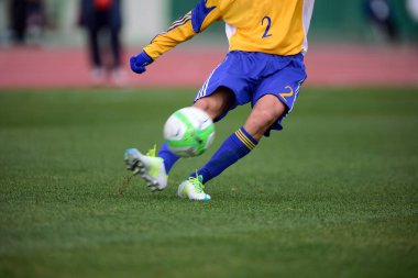Bir futbolcu sahada futbol topunu tekmeliyor.