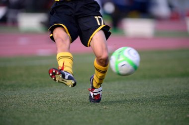 Bir futbolcu sahada futbol topunu tekmeliyor.