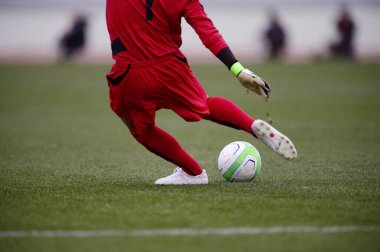 Bir futbolcu sahada futbol topunu tekmeliyor.