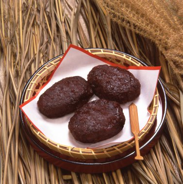 Üç koyu oval köfte örülmüş sepetin içinde kağıt üzerinde dinleniyor.