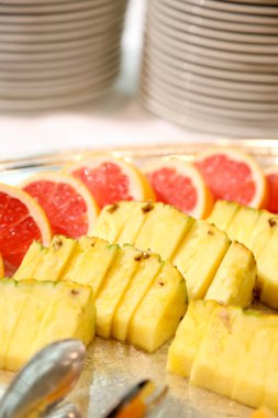 Sliced pineapple and grapefruit arranged neatly beside stacked plates