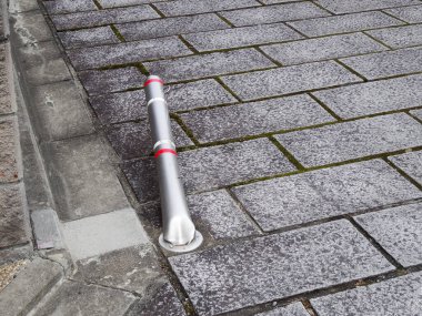 Gri taş kaldırım boyunca uzanan metal bir direk.