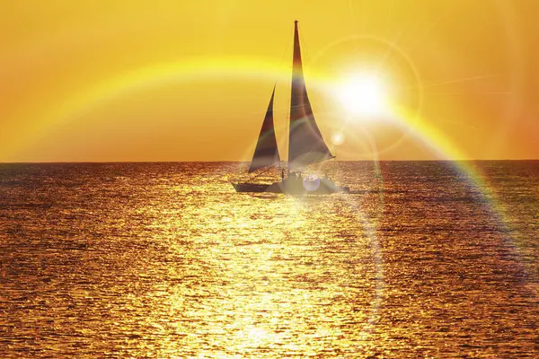 Dalgalar üzerinde yelken açan yatıyla denizin üzerinde güzel bir gün batımı.              