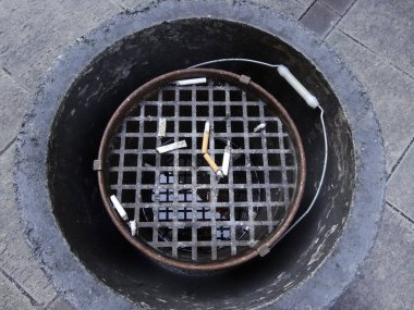 Şehir metal ızgarasının içinde sigara izmaritleri duruyor.