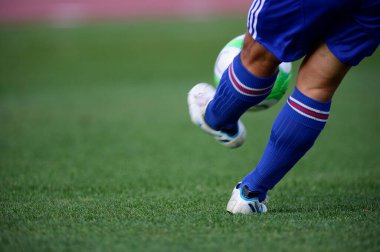 Bir futbolcu sahada futbol topunu tekmeliyor.