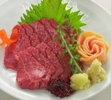 İnce dilimlenmiş çiğ biftekli sashimi garnitür yapraklarının yanında.