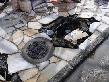 Kırık taşlar ve rögar kapağı görünüyor.