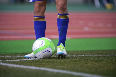 Bir futbolcu sahada futbol topunu tekmeliyor.