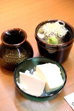 Çorba ve yeşil soğan dolu kasenin yanında taze tofu dilimleri.