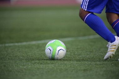 Bir futbolcu sahada futbol topunu tekmeliyor.