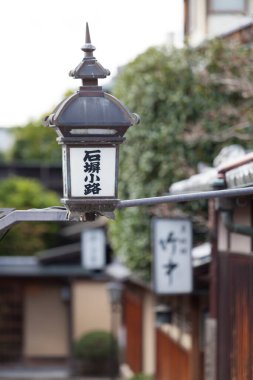 Geleneksel fener ahşap binaların ve yeşilliklerin yanında asılı.