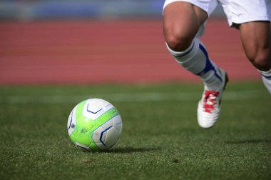 Bir futbolcu sahada futbol topunu tekmeliyor.