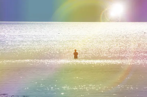 a man stands in sea during sunset