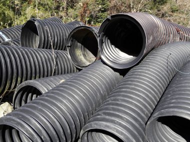 Yığılmış siyah drenaj boruları dışarıda yerde yatıyor.