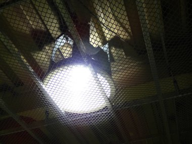 Metal ağ ızgarasının arkasındaki parlak tavan ışığı