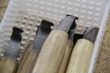 Kapalı çekim beyaz plastik kabın içinde duran ahşap oyma araçlarını gösteriyor