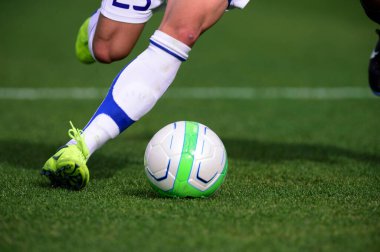 Bir futbolcu sahada futbol topunu tekmeliyor.