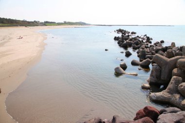 Beton tetrapodlar sakin mavi suyun yanında kumlu plajı kaplıyor.