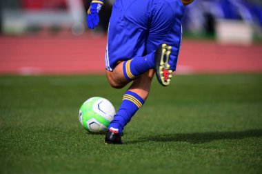 Bir futbolcu sahada futbol topunu tekmeliyor.