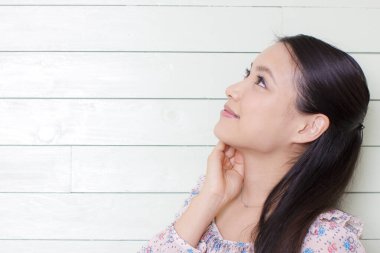 Uzun saçlı ve çiçekli elbiseli genç Asyalı kadın beyaz tahta duvara karşı poz veriyor. 