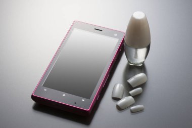 Cep telefonu ve kozmetik ürünlerinin yakın plan görüntüsü, gri arka planda tırnak cilası.          